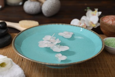 Photo of Bowl of water with flowers and different spa supplies on table, closeup