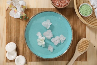 Photo of Bowl of water with flowers and different spa supplies on wooden table, flat lay