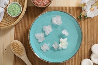 Photo of Bowl of water with flowers and different spa supplies on wooden table, flat lay