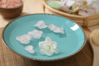 Photo of Bowl of water with flowers and different spa supplies on table, closeup