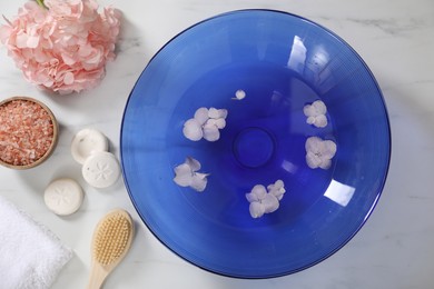 Photo of Bowl of water with flowers and different spa supplies on white marble table, flat lay