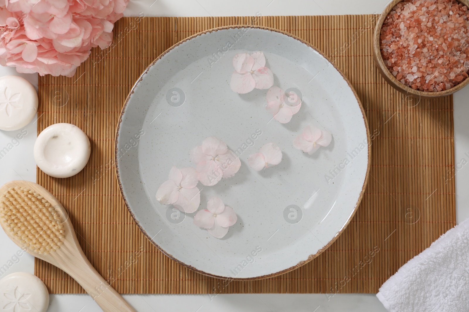 Photo of Bowl of water with flowers and different spa supplies on white table, flat lay