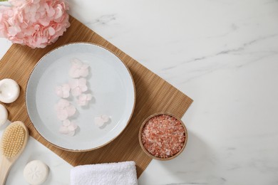 Photo of Bowl of water with flowers and different spa supplies on white marble table, flat lay. Space for text