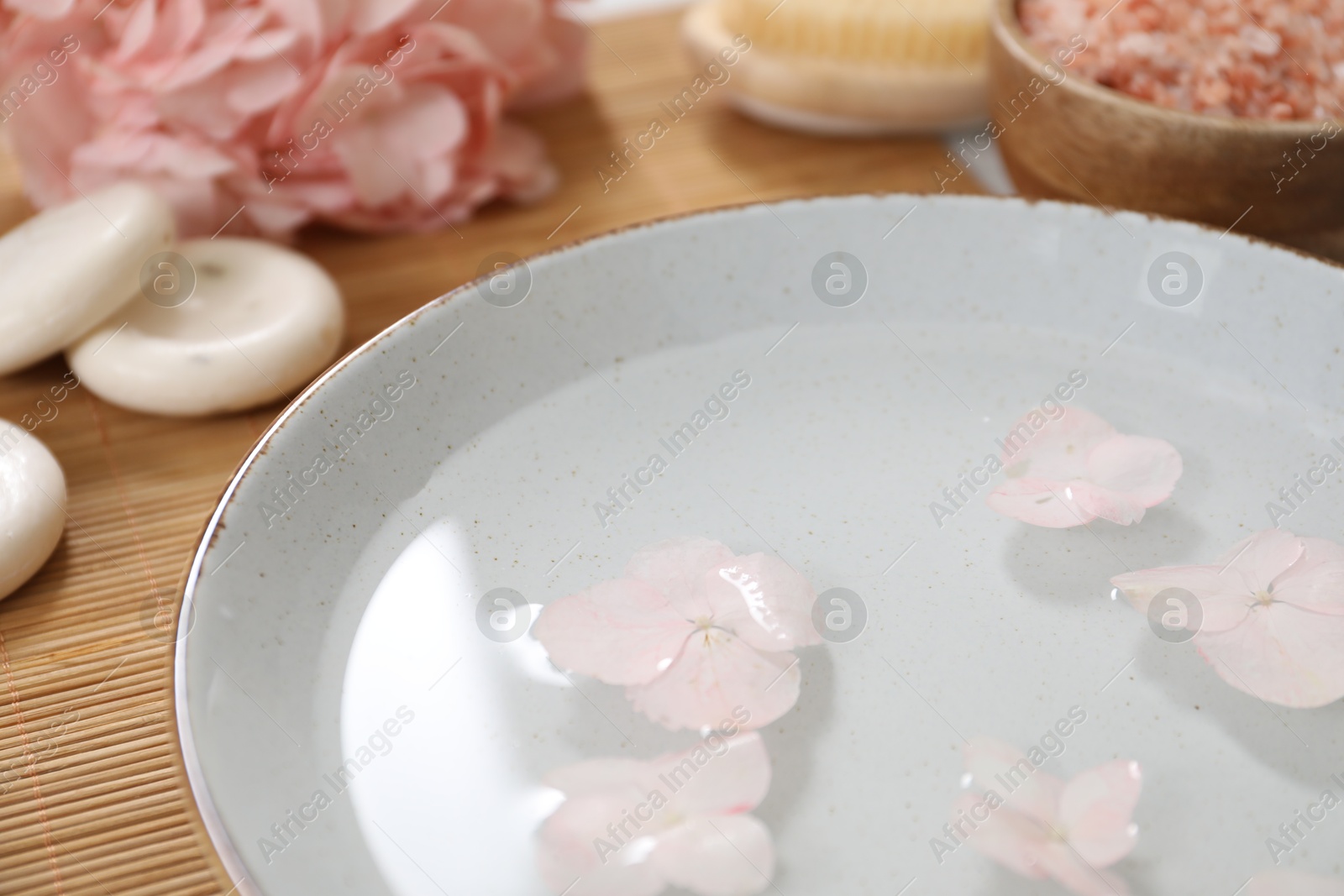 Photo of Bowl of water with flowers and different spa supplies on table, closeup