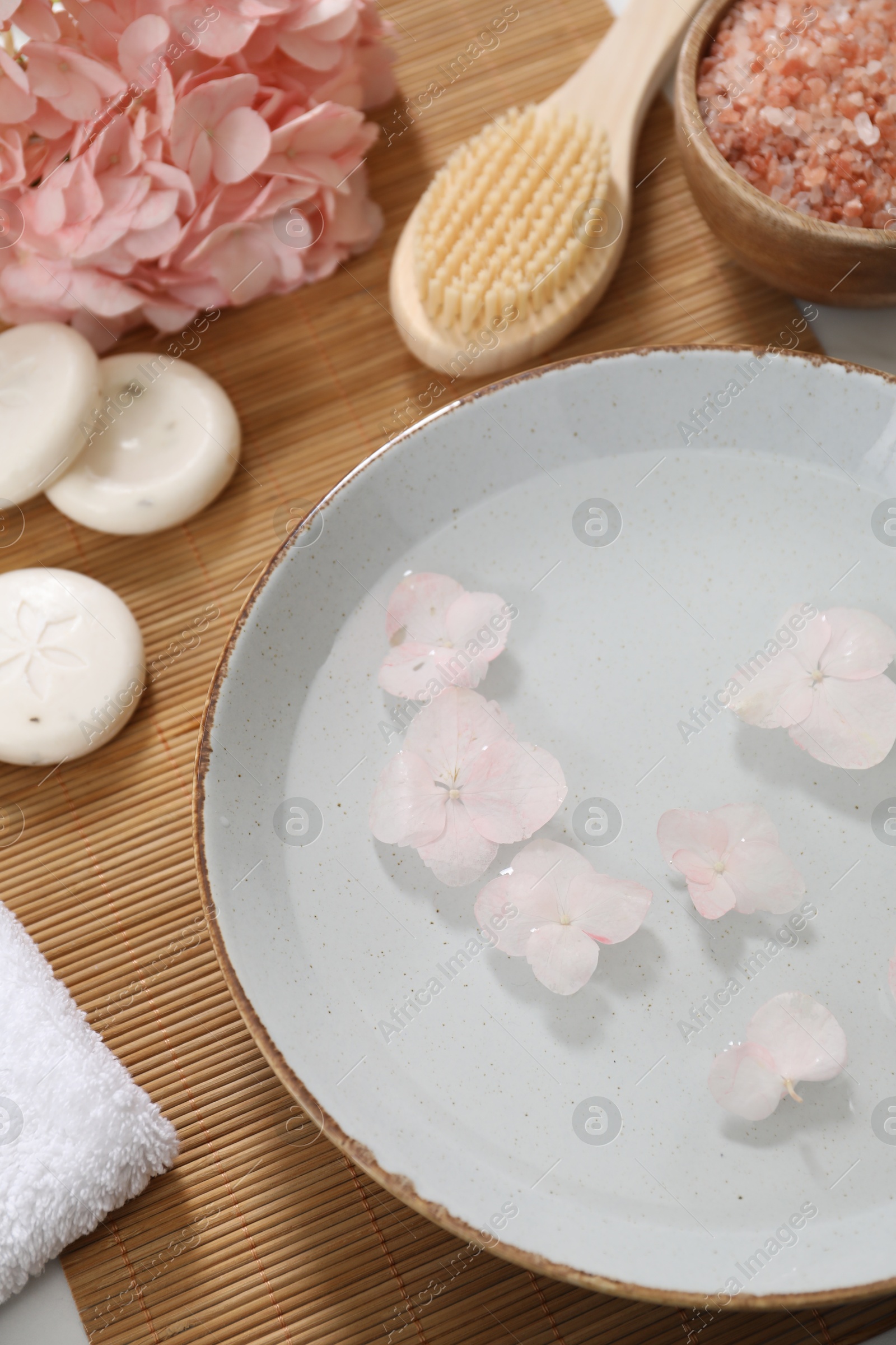 Photo of Bowl of water with flowers and different spa supplies on table, above view