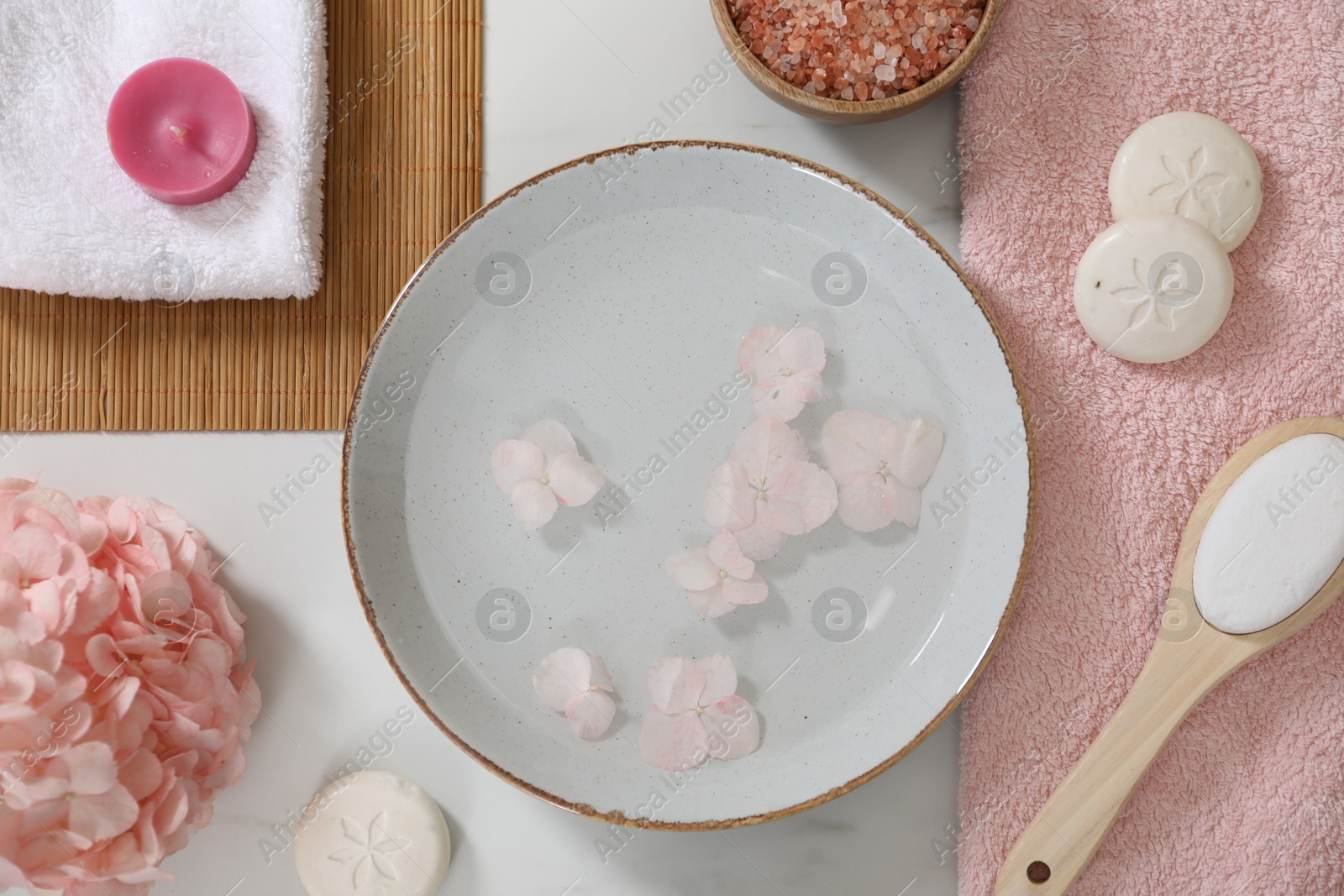 Photo of Bowl of water with flowers and different spa supplies on white marble table, flat lay