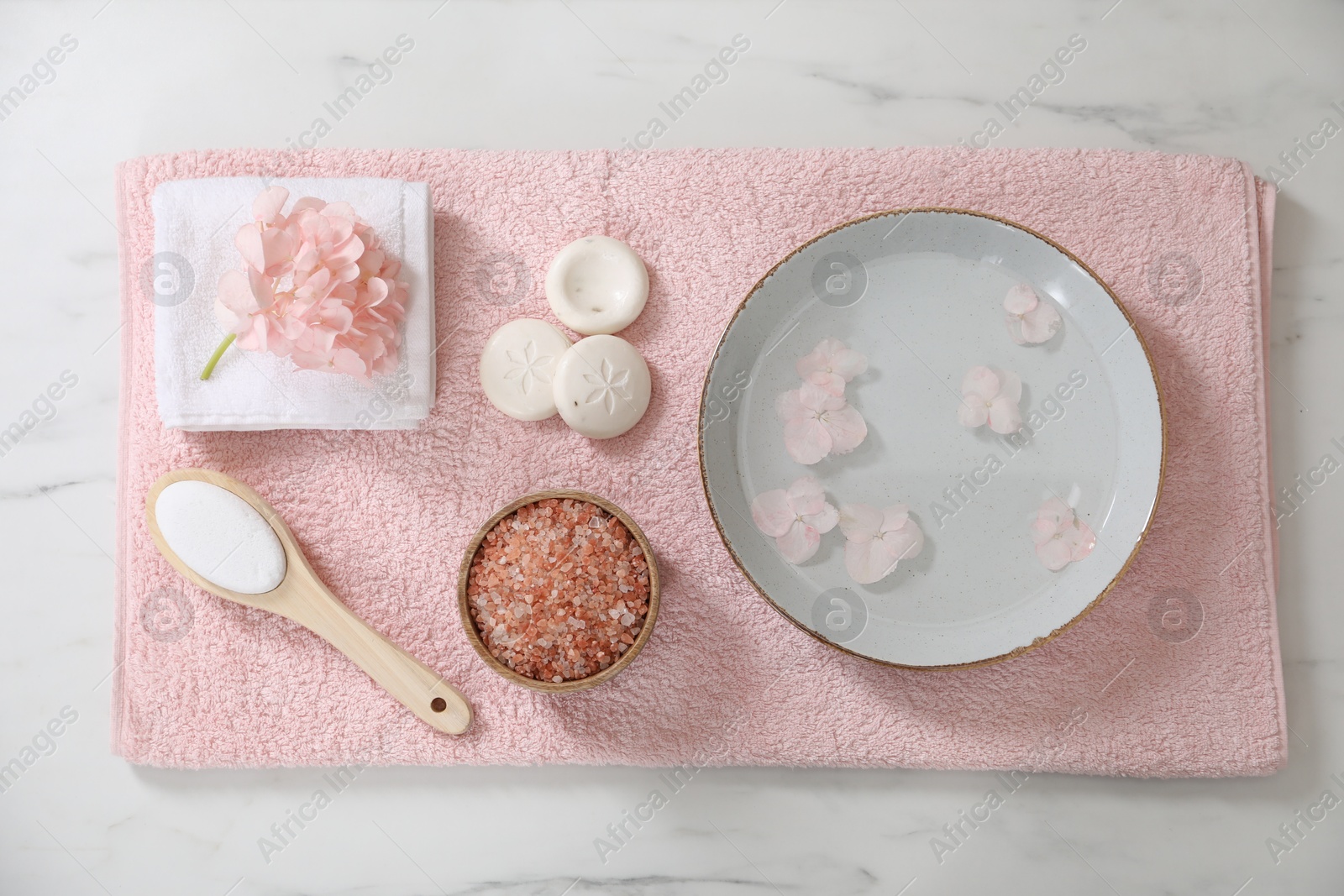 Photo of Bowl of water with flowers and different spa supplies on white marble table, flat lay