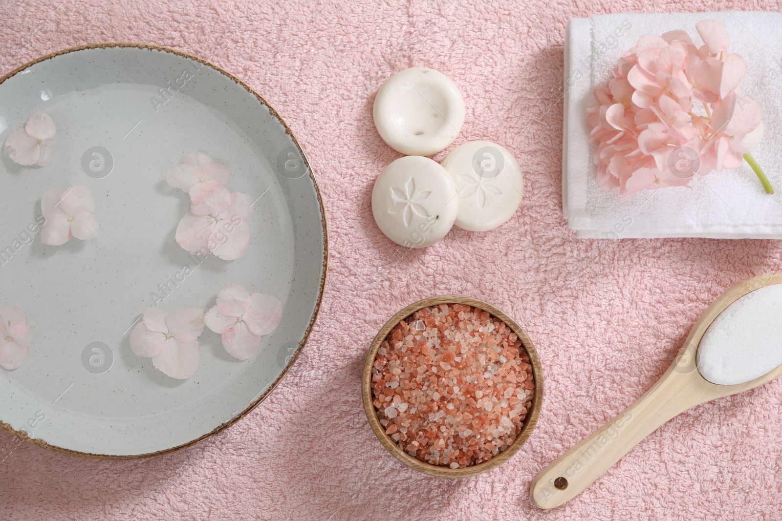 Photo of Bowl of water with flowers and different spa supplies on pink towel, flat lay