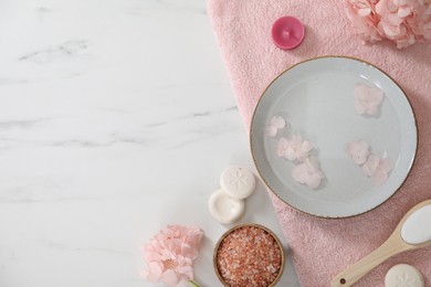 Photo of Bowl of water with flowers and different spa supplies on white marble table, flat lay. Space for text