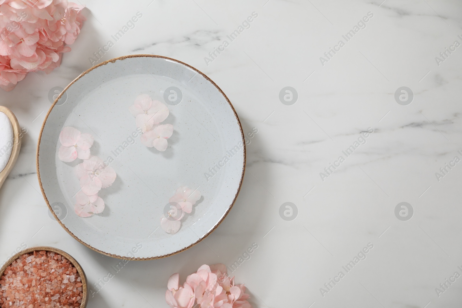 Photo of Bowl of water with flowers and different spa supplies on white marble table, flat lay. Space for text