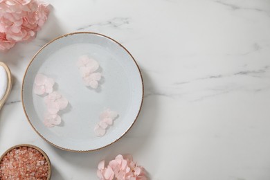 Photo of Bowl of water with flowers and different spa supplies on white marble table, flat lay. Space for text