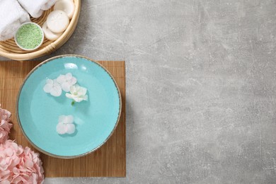 Photo of Bowl of water with flowers and different spa supplies on grey table, flat lay. Space for text