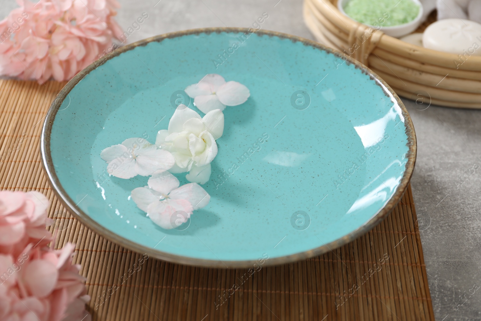 Photo of Bowl of water with flowers and different spa supplies on grey table, closeup