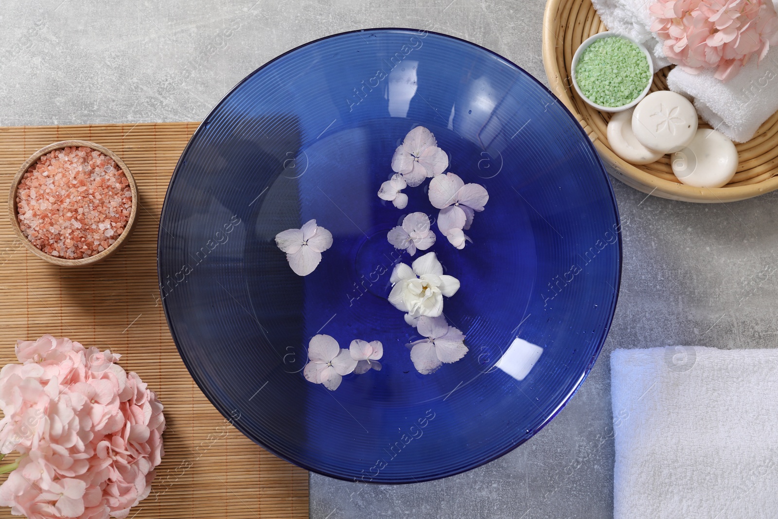 Photo of Bowl of water with flowers and different spa supplies on grey table, flat lay