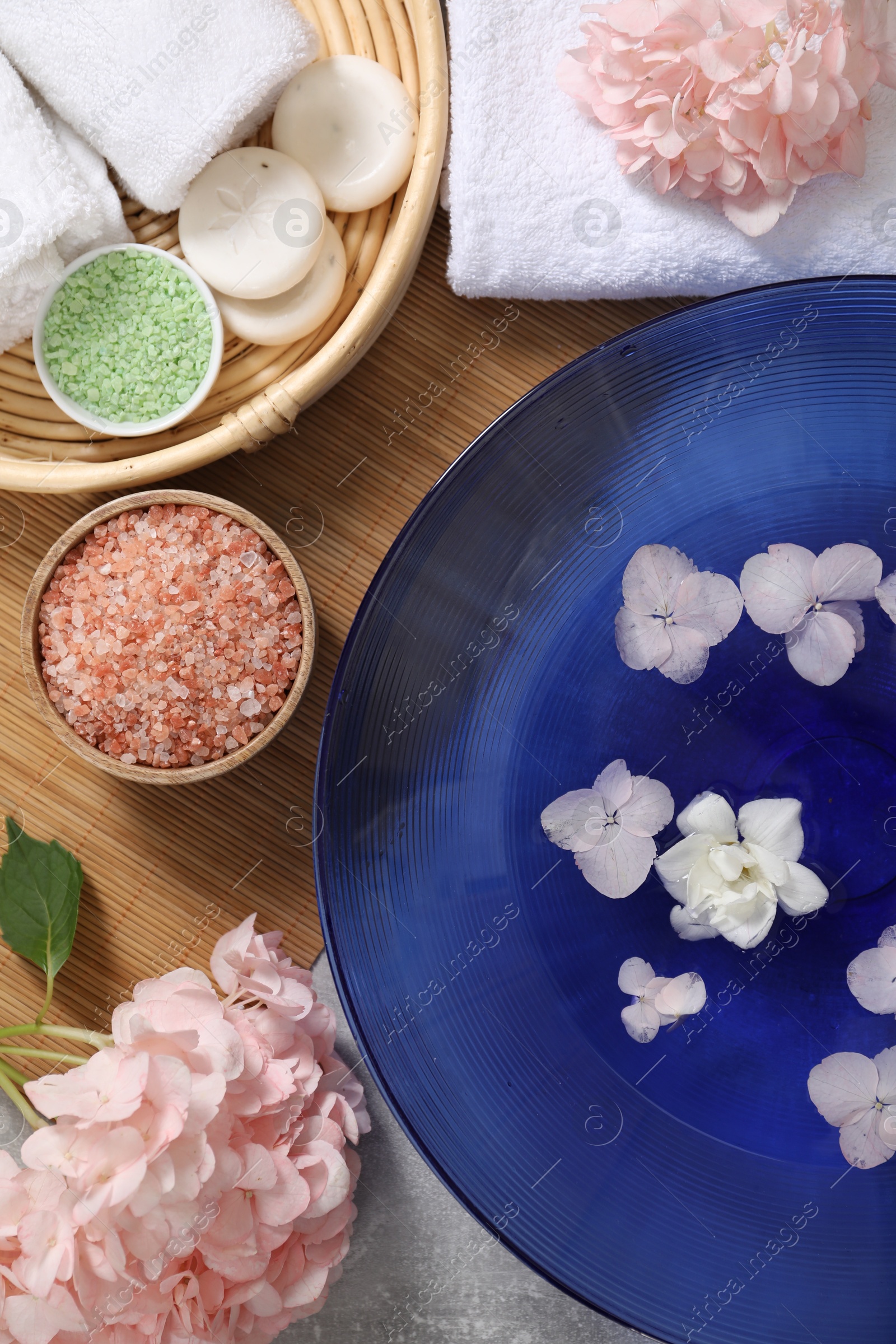 Photo of Bowl of water with flowers and different spa supplies on grey table, flat lay