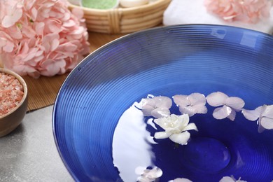 Photo of Bowl of water with flowers and sea salt on grey table, closeup. Spa treatment