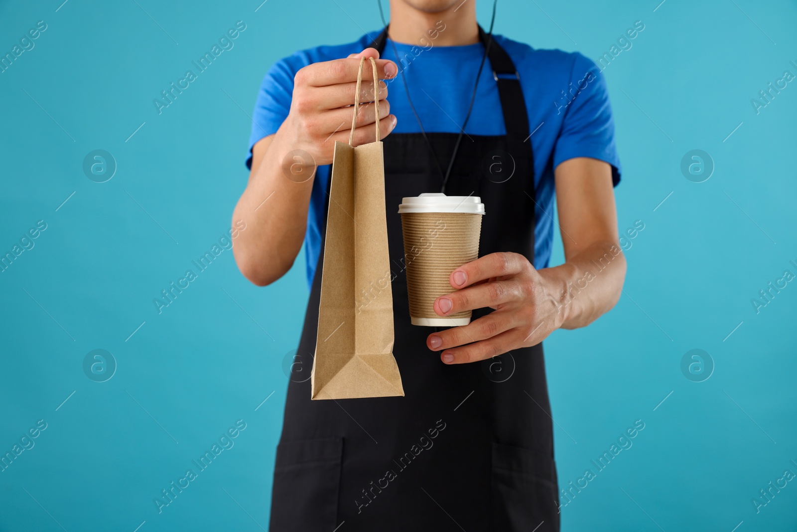 Photo of Fast-food worker with paper bag and cup on light blue background, closeup