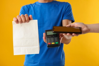 Photo of Fast-food worker taking payment from client via terminal on orange background, closeup