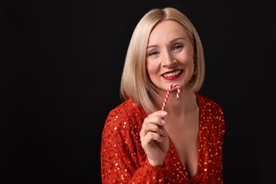 Photo of Smiling woman with perfect makeup holding Christmas candy cane on black background. Space for text