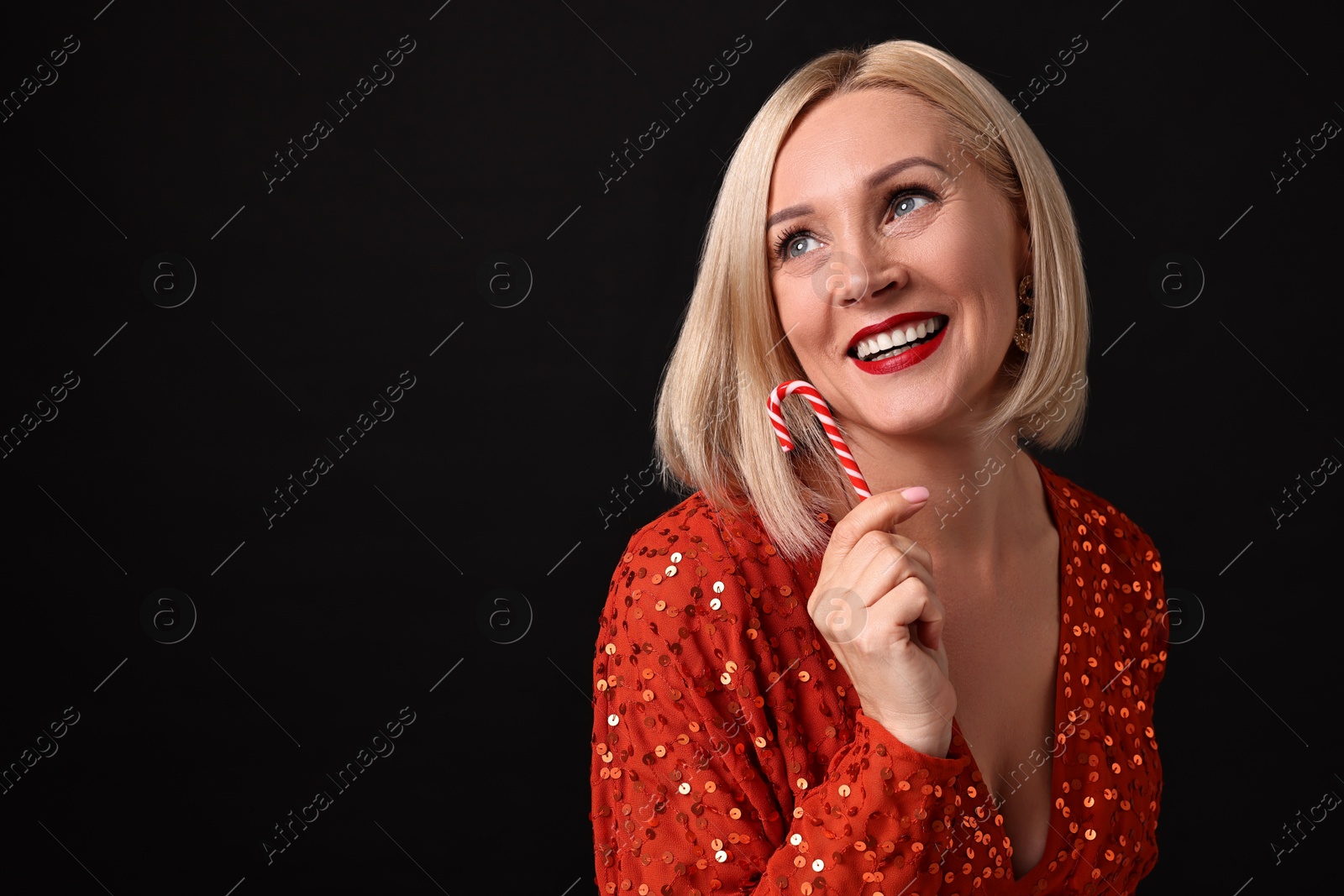 Photo of Smiling woman with perfect makeup holding Christmas candy cane on black background. Space for text