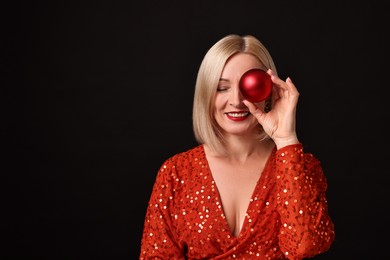 Photo of Smiling woman with perfect makeup holding Christmas bauble on black background. Space for text