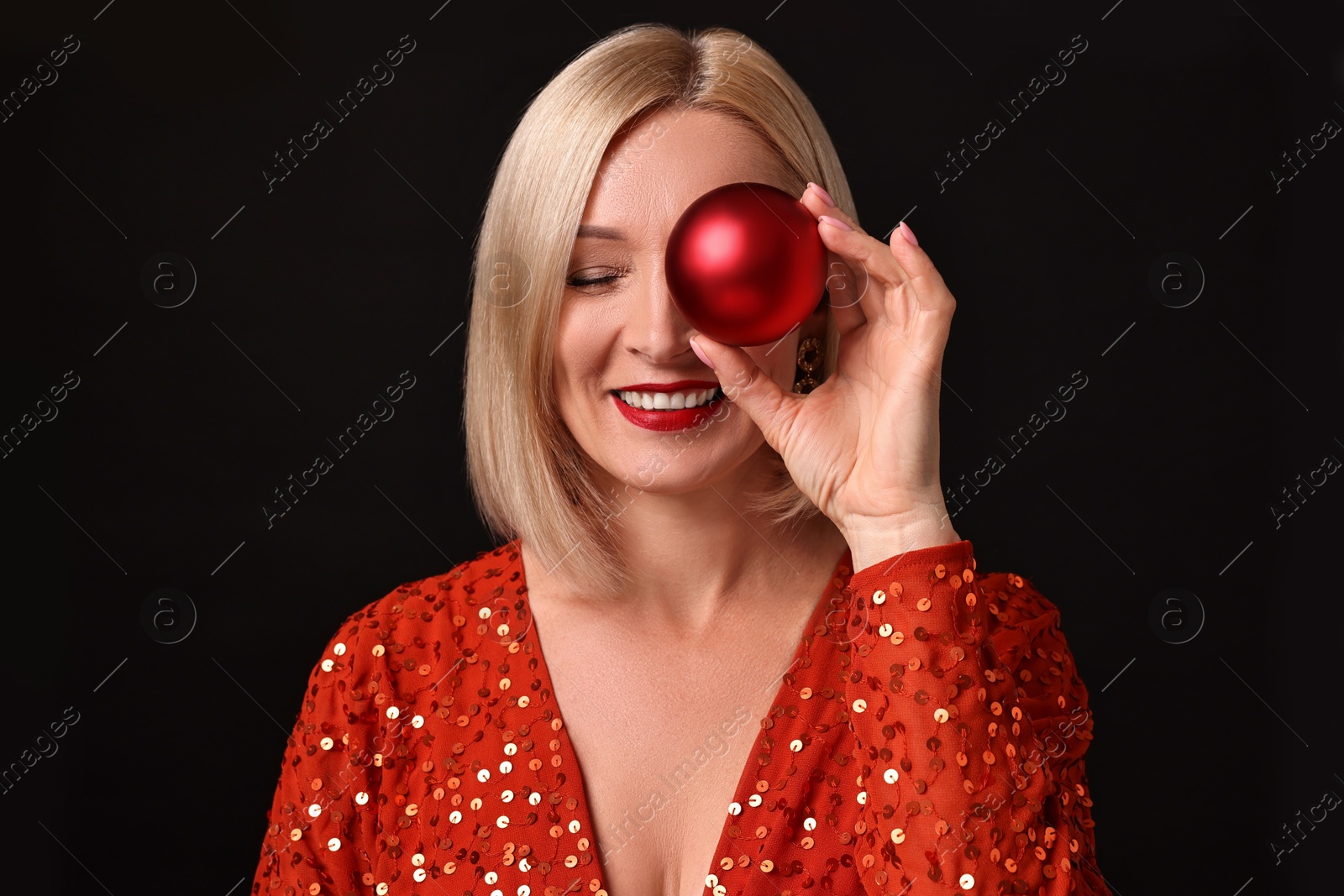 Photo of Smiling woman with perfect makeup holding Christmas bauble on black background