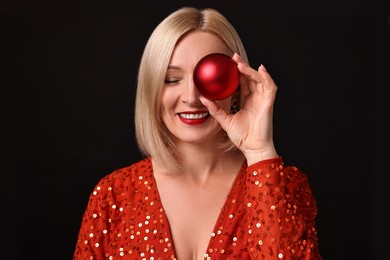 Photo of Smiling woman with perfect makeup holding Christmas bauble on black background