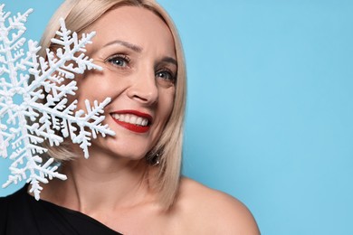 Photo of Smiling woman with decorative snowflake on light blue background, space for text. Christmas celebration