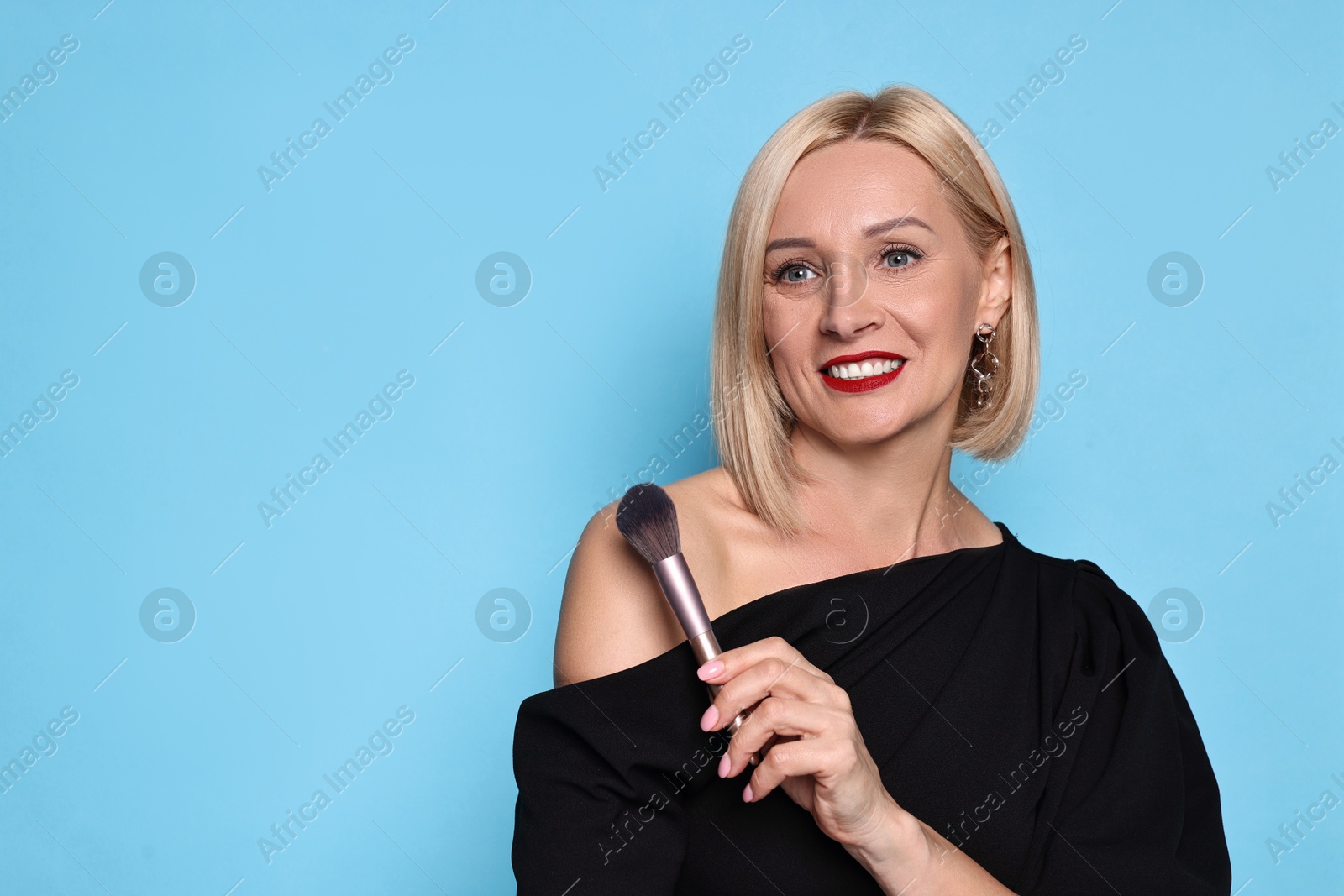 Photo of Smiling woman with makeup brush on light blue background. Space for text