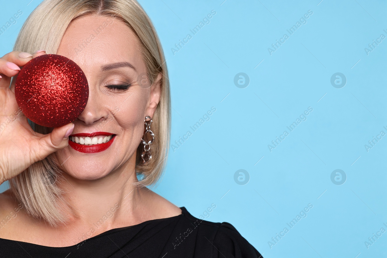 Photo of Smiling woman with Christmas bauble on light blue background. Space for text