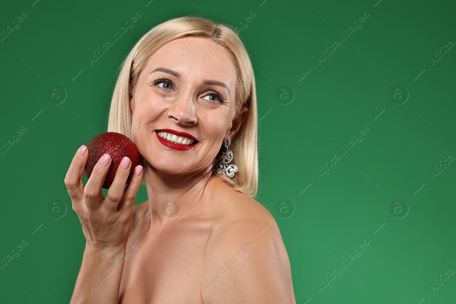 Photo of Smiling woman with perfect makeup and Christmas bauble on green background. Space for text