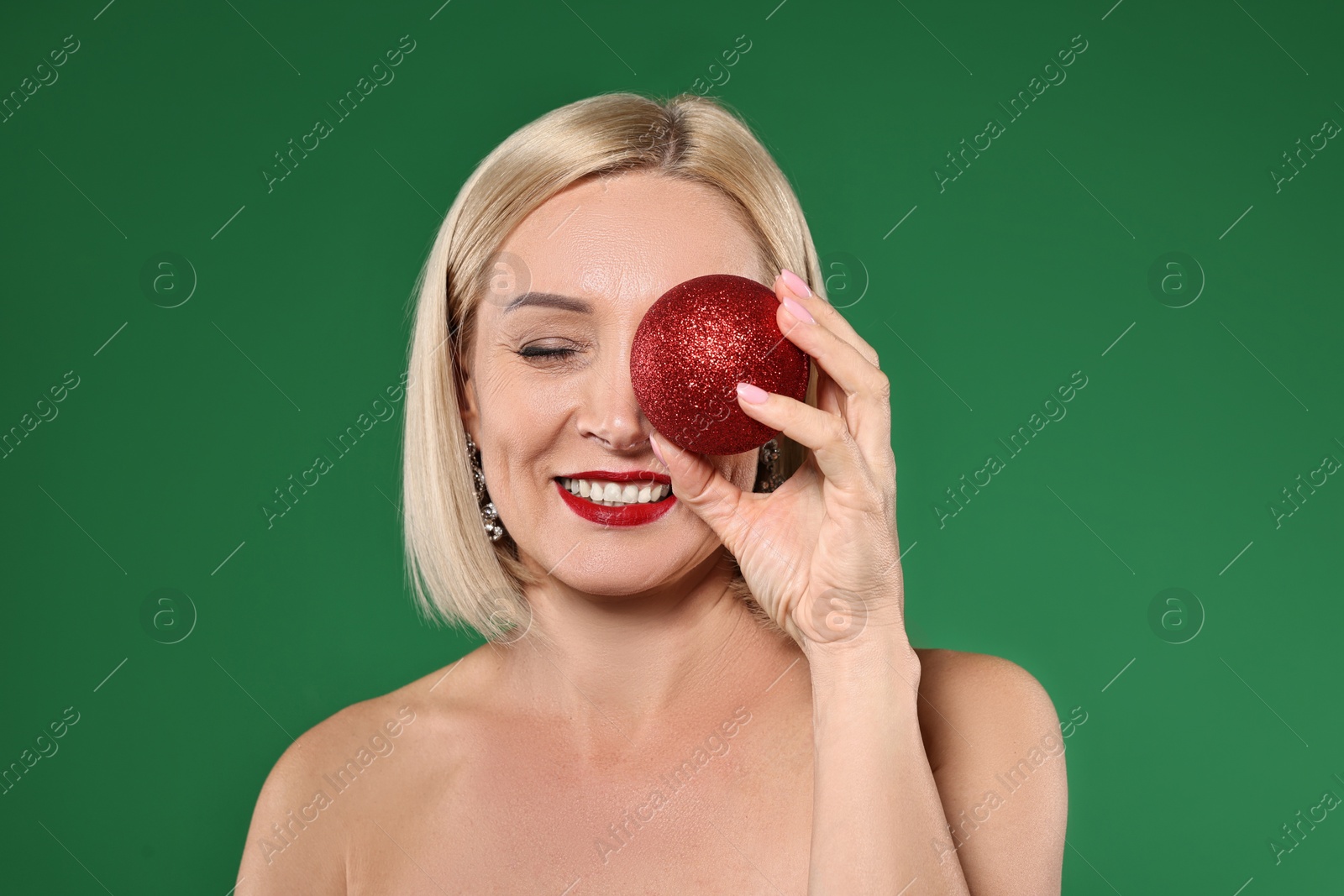 Photo of Smiling woman with perfect makeup and Christmas bauble on green background