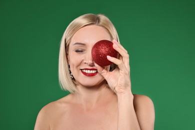 Smiling woman with perfect makeup and Christmas bauble on green background