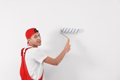 Photo of Smiling handyman painting wall with roller indoors