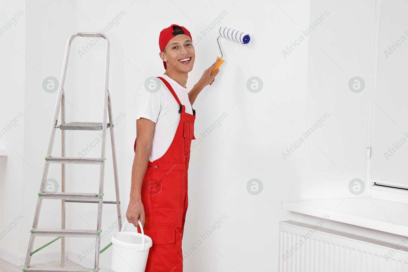 Photo of Smiling handyman painting wall with roller indoors