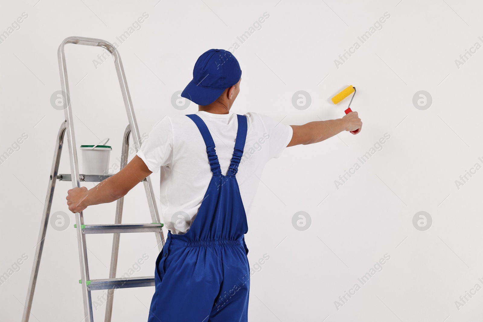 Photo of Male handyman painting wall with roller indoors, back view. Space for text