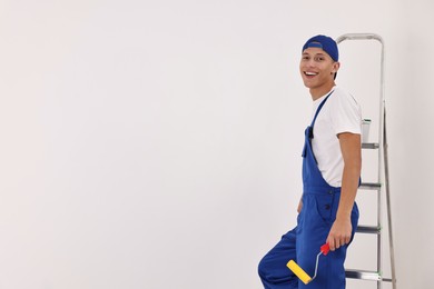 Smiling handyman with paint roller near white wall. Space for text