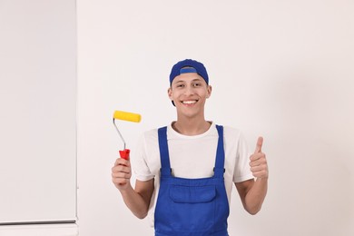 Photo of Smiling handyman with paint roller showing thumbs up indoors