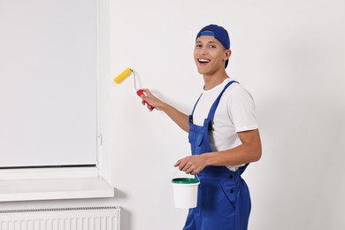 Photo of Smiling handyman painting wall with roller indoors