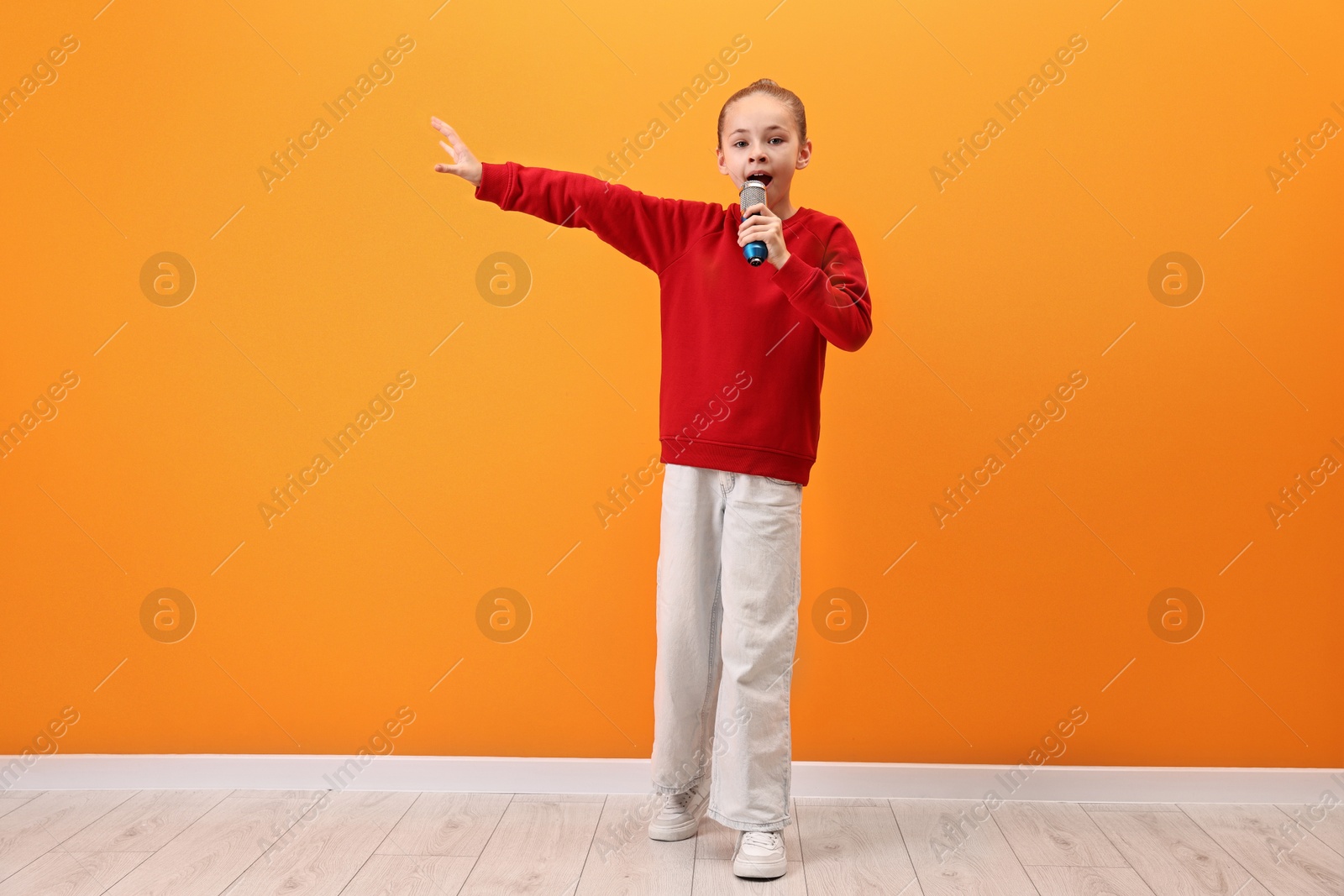 Photo of Little girl with microphone singing near orange wall