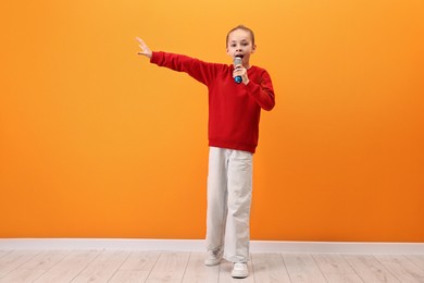 Photo of Little girl with microphone singing near orange wall