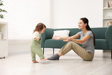 Photo of First steps. Mother supporting daughter while she learning to walk at home