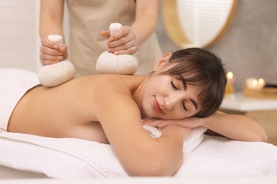 Young woman receiving massage with herbal bags in spa salon