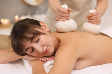 Photo of Young woman receiving massage with herbal bags in spa salon