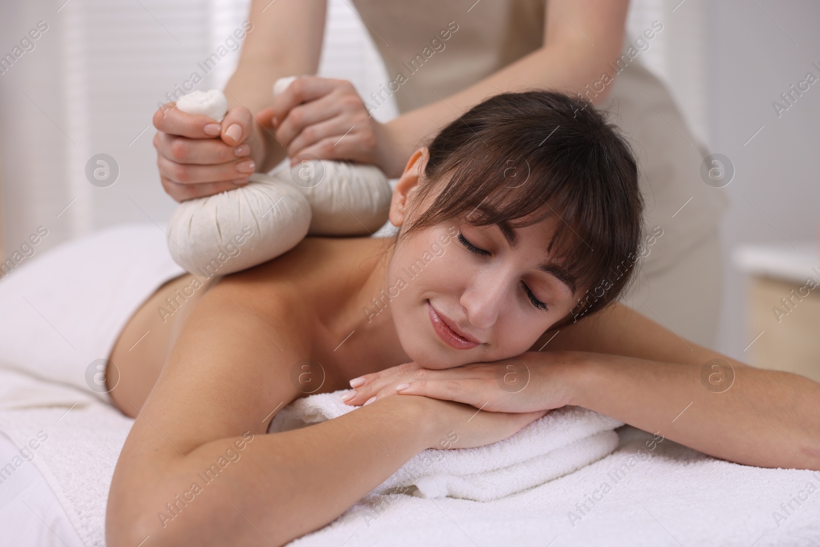 Photo of Young woman receiving massage with herbal bags in spa salon