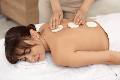 Photo of Young woman receiving hot stone massage in spa salon