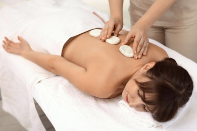 Photo of Young woman receiving hot stone massage in spa salon