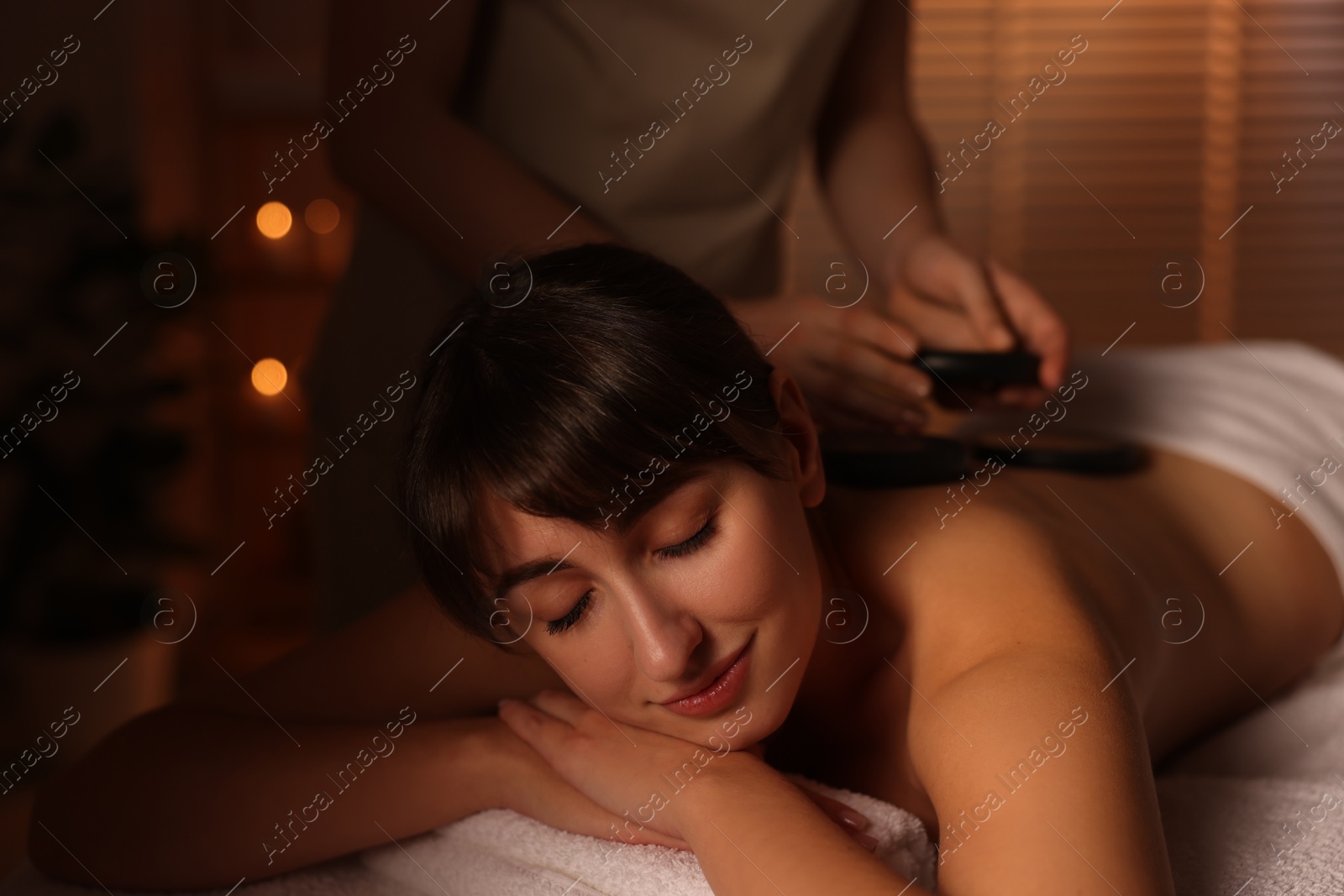 Photo of Young woman receiving hot stone massage in spa salon