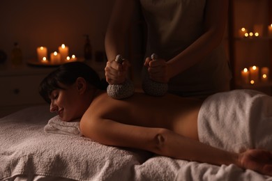 Photo of Young woman receiving back massage with herbal bags in spa salon