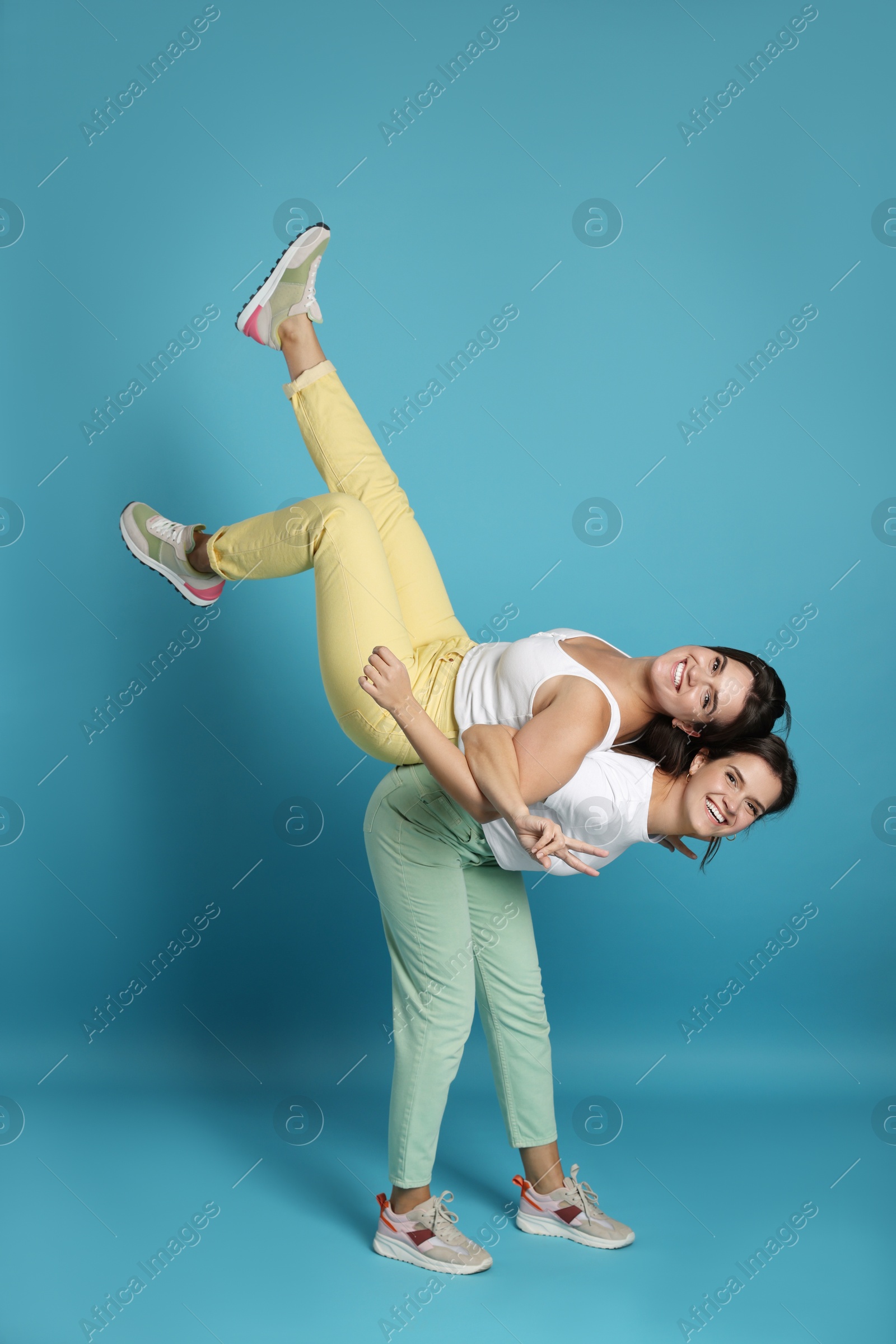 Photo of Beautiful twin sisters having fun on light blue background